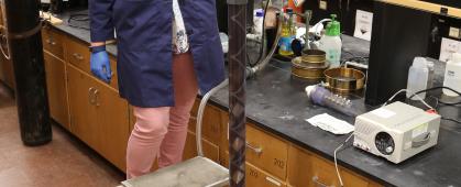 Teagan Leitzke, a Ph.D. student at Montana Tech, pours a slurry of magnetite and water into the continuous flow metal recovery system. The slurry flows through the static mixer column to a magnet, where the magnetite is collected, and water continues to flow out of the system. Photo credit: Amanda Badovinac